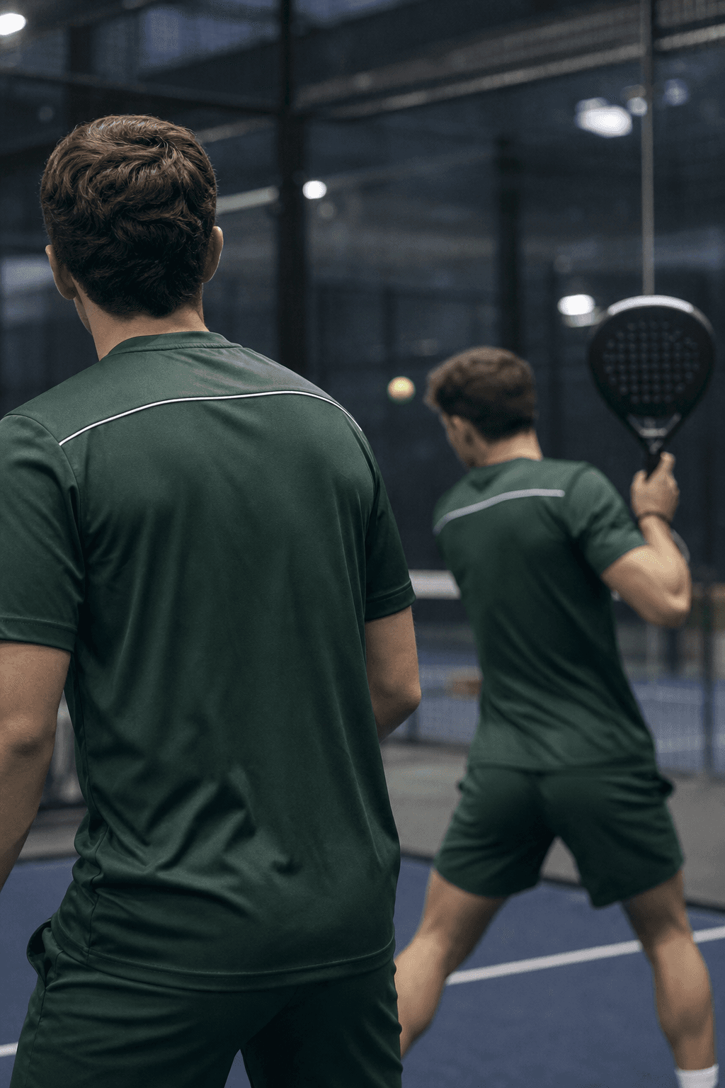 Two padel players in matching club shirts during a rally on an indoor court